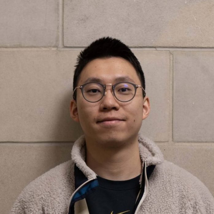 Portrait of a person in a hoodie standing against a concrete block wall.