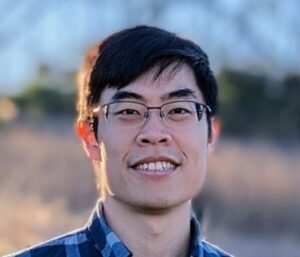 Portrait of a person outdoors wearing a blue plaid shirt; blurred landscape background