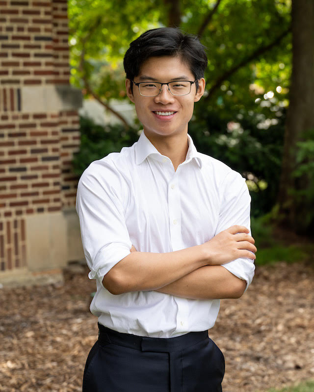 Outdoor portrait of a man with arms crossed in a white shirt near a brick wall