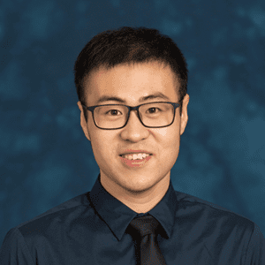 Studio headshot of a person in a dark collared shirt against a blue background