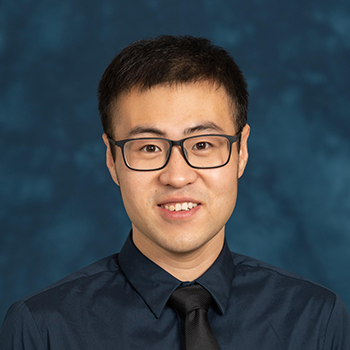 Studio headshot of a person in a dark collared shirt against a blue background