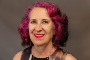 Studio headshot of a person with short bright-red hair against a dark background