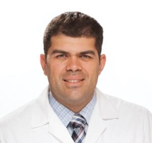 Studio headshot of a person in a white coat and tie against a white background
