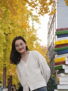 Woman smiling at camera, trees and building behind her.