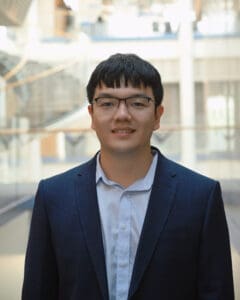 Man smiling at camera, academic building behind him.