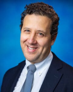 Studio headshot of a person in a suit against a blue background.