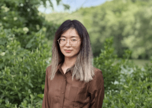 Outdoor portrait of a woman standing in greenery.