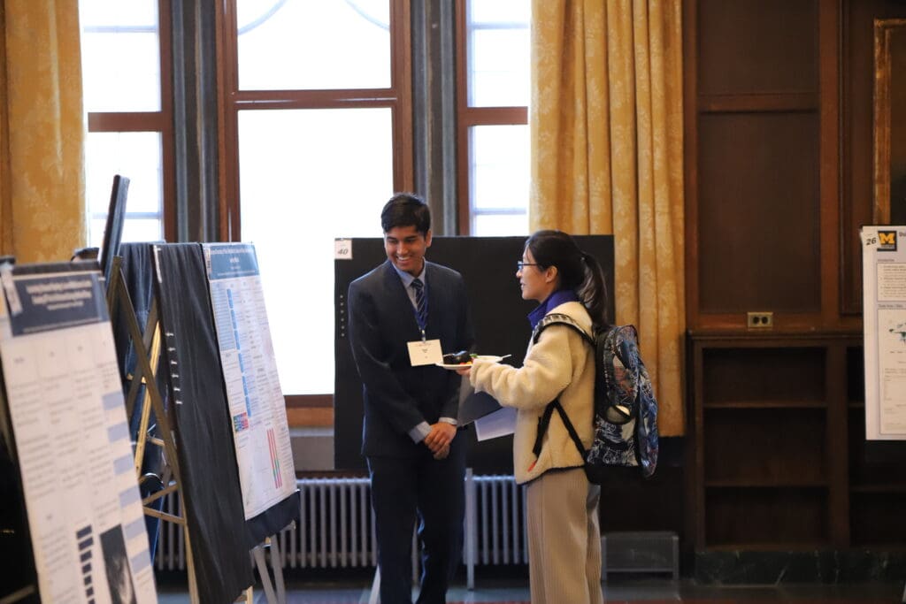 A person standing in front of their poster presenting to an onlooker