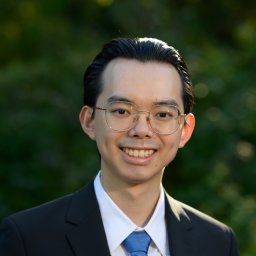 Man in a suit standing against a blurred background of greenery