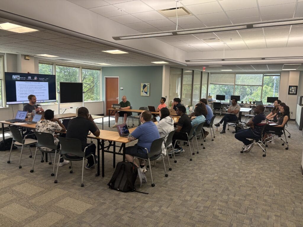 Researchers sitting at a large table in a large workspace with their laptops.
